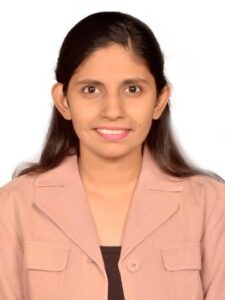 Porträt einer jungen Frau mit langen dunklen Haaren, beigem Blazer und dunklem Oberteil vor hellem Hintergrund.