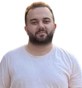 Mann mit dunklem Bart und kurzen Haaren trägt weißes T-Shirt vor hellem Hintergrund.